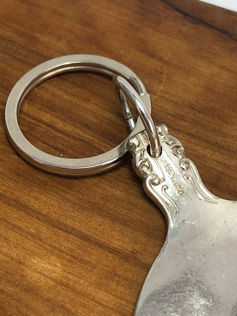 May include: Silver spoon keychain with a decorative handle and a ring attached. The spoon has the word "Pat. No." engraved on the back.