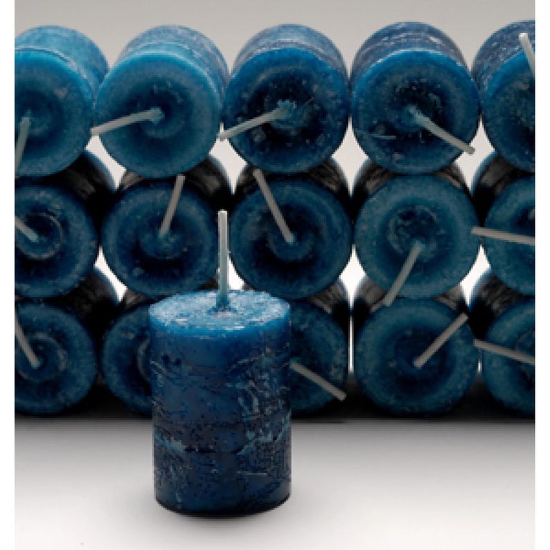 Several teal balanced energy votive candles are lying on their side facing forward, with one standing upright on a white table.