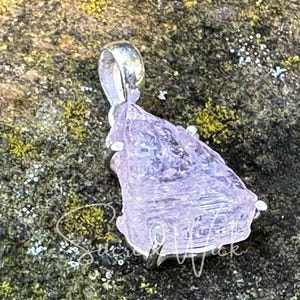 aa+ quality pink kunzite pendant lying at an angle on a rock showing depth and color