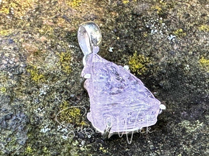 aa+ quality pink kunzite pendant lying at an angle on a rock showing depth and color