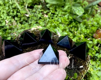 May include: Seven black obsidian pyramids of various sizes, some are on a bed of moss and one is being held in a hand.