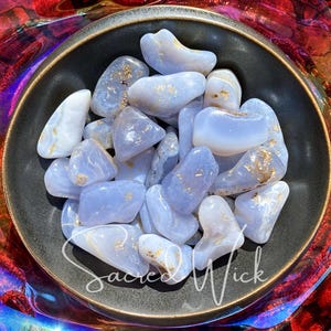 An assortment of tumbled blue chalcedony stones in a bronze bowl basking in sunlight, showcasing their soft, soothing blue tones and gentle energy known for promoting calm, emotional balance, clear communication, and spiritual connection.