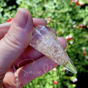 May include: A clear quartz crystal pendulum with a silver chain. The crystal is filled with small, white and gold flecks.