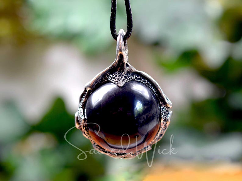 One black obsidian scrying ball pendant necklace hangs with greenery in the background.