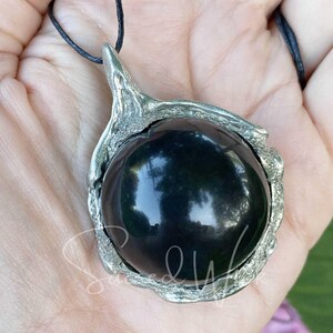 One black obsidian scrying ball pendant necklace lies on an open palm to display the size.