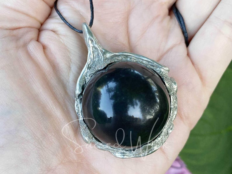 One black obsidian scrying ball pendant necklace lies on an open palm to display the size.