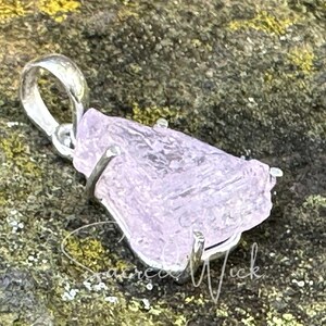 close up of pink kunzite nugget pendant set in sterling silver lying atop a rock at an angle to show the unique texture of the all-natural aa+ quality kunzite nugget.