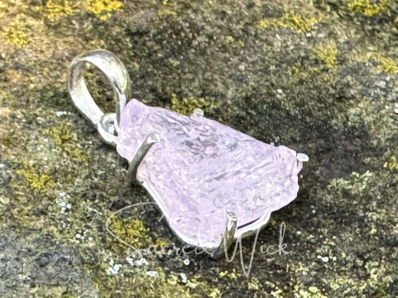 close up of pink kunzite nugget pendant set in sterling silver lying atop a rock at an angle to show the unique texture of the all-natural aa+ quality kunzite nugget.