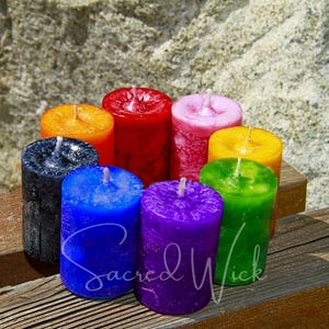 A circle of colorful handmade votive candles stand on a wooden slat bench with a rockface in the background.