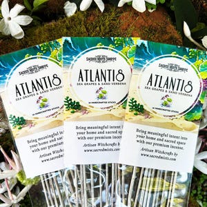 May include: Three packages of incense sticks with a beach scene and the text "ATLANTIS SEA GRAPES & SAND VERBENA" on the front. The text "SACRED MISTS SHOPPE" is also on the front of the packages. The packages are surrounded by white flowers.