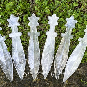 Six clear quartz crystal athames with star handles lying on greenery with a rock at the bottom.
