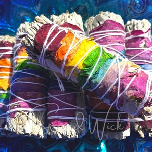 May include: A bundle of white sage smudge sticks wrapped with colorful flower petals and white string. The petals are arranged in a rainbow pattern.