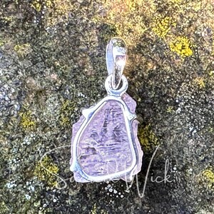 raw aa+ pink kunzite pendant lying on a rock showing the back of the sterling silver setting and the natural texture of the stone