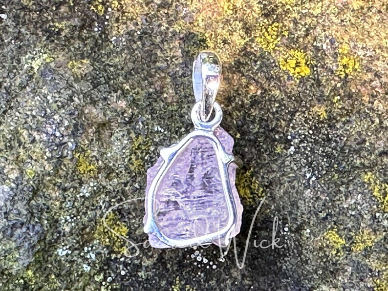 raw aa+ pink kunzite pendant lying on a rock showing the back of the sterling silver setting and the natural texture of the stone