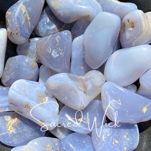 A close up of an assortment of tumbled blue chalcedony stones in a bronze bowl basking in sunlight, showcasing their soft, soothing blue tones and gentle energy known for promoting calm, emotional balance, clear communication, and spiritual connection.