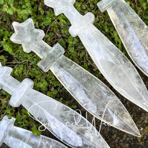 Macro close-up of six clear quartz crystal athames on greenery with stone accent, showing fine detail of carving.