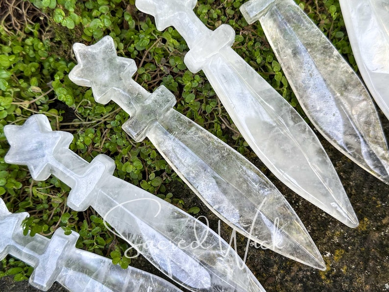 Macro close-up of six clear quartz crystal athames on greenery with stone accent, showing fine detail of carving.