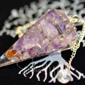 May include: A clear quartz crystal pendulum with a silver chain and a clear crystal bob. The pendulum is filled with small amethyst crystals.
