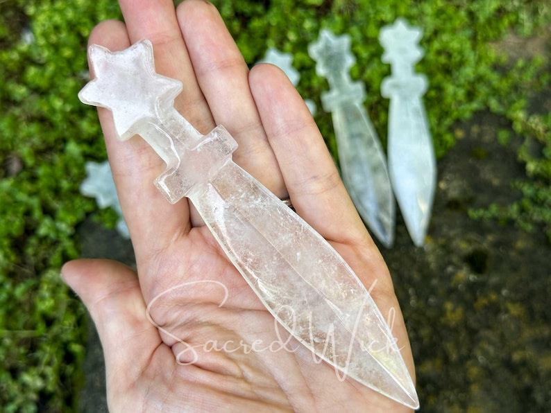 Clear quartz crystal athame resting on open palm, showing size with more athames on greenery in the background.