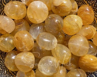 May include: A collection of tumbled Citrine stones in various shades of yellow and orange. The stones are smooth and polished, with a translucent appearance.