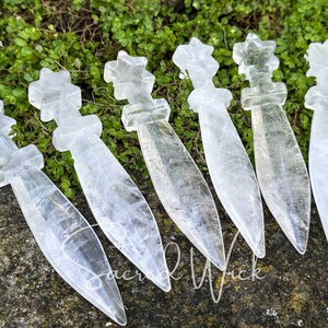 Group of six clear quartz athames with star handles lying on greenery and stone, angled to show dimension and detail.