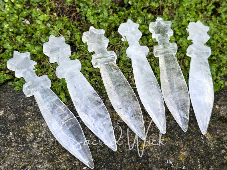 Group of six clear quartz athames with star handles lying on greenery and stone, angled to show dimension and detail.