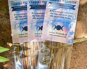 May include: Three packs of incense sticks with labels that read "Charge of the Goddess" and "Charge of the God". The labels feature a triple moon symbol and the text "Parma Violet and Sweet Katsura 10 Handcrafted Sticks". The incense sticks are packaged in clear plastic.