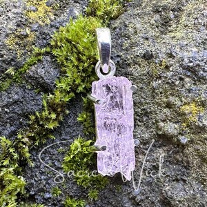 pink kunzite natural and raw nugget crystal pendant handset in sterling silver resting atop a rock showing the aa+ quality color and clarity
