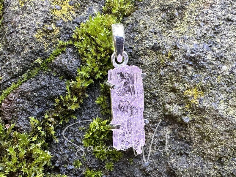 pink kunzite natural and raw nugget crystal pendant handset in sterling silver resting atop a rock showing the aa+ quality color and clarity