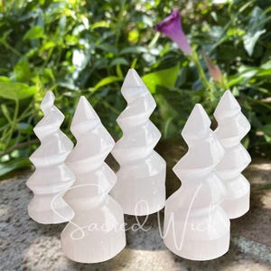 May include: Five white selenite crystal trees, each with a unique spiral shape, arranged on a gray surface. The crystals are smooth and polished, with a soft, milky white color.