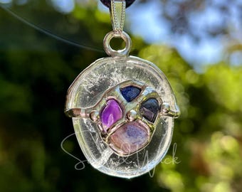 May include: A silver pendant with a clear quartz crystal, featuring a caged design with amethyst, blue lace agate, and blue sapphire stones.