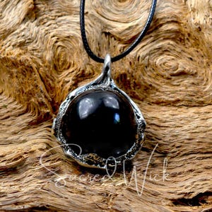 One black obsidian scrying ball pendant necklace rests on a piece of wood.