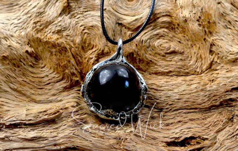 One black obsidian scrying ball pendant necklace rests on a piece of wood.