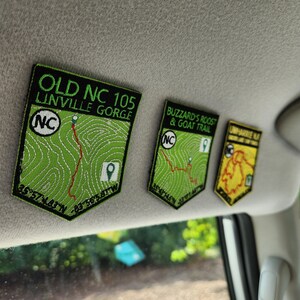 May include: Three green and black embroidered patches with the text "Old NC 105 Linville Gorge", "Buzzard's Roost & Goat Trail", and "Uwharrie Nat'l Forest" with a map of each location and coordinates.