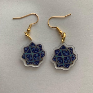 May include: A pair of gold dangle earrings with a blue and gold geometric design. The design is reminiscent of a 20-sided die.
