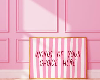 May include: A framed print with a pink and white striped design and the text "WORDS OF YOUR CHOICE HERE" in red. The frame is a light brown color. The background is a pink wall with molding and a wooden floor.