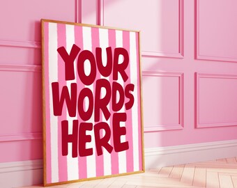 May include: A framed print with a gold border, leaning against a pink wall. The print features vertical pink and white stripes and the words "YOUR WORDS HERE" in bold red letters. The room has a pink wainscoting and a wooden floor.