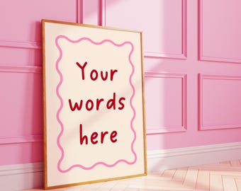 May include: A framed print with the text "Your words here" in red, set against a cream background with a pink wavy border. The frame is leaning against a pink wall and floor.