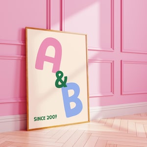 May include: A framed print with the letters "A" in pink and "B" in blue, separated by a green ampersand. The text "SINCE 2007" is printed in green at the bottom. The artwork is displayed against a pink wall.