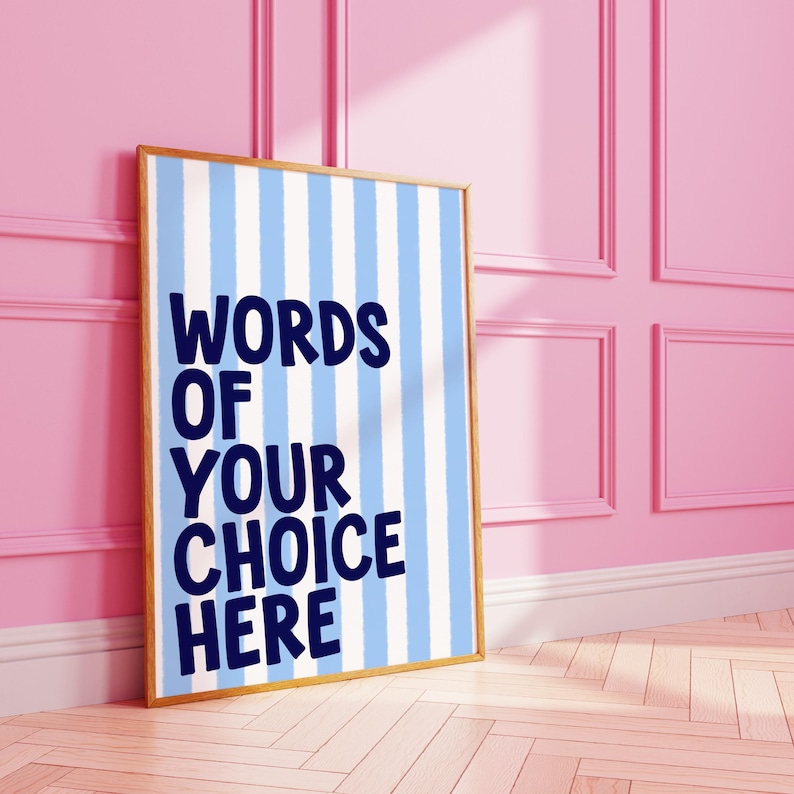 May include: A framed poster with a light blue and white striped background. The poster has the words "WORDS OF YOUR CHOICE HERE" in dark blue. The frame is a light brown color. The poster is leaning against a pink wall.