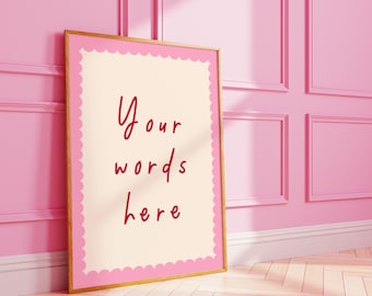 May include: A framed print with the text "Your words here" in a red script font. The print has a scalloped pink border and a gold frame, leaning against a pink wall. The room has a light wood floor and a pink wainscoting.
