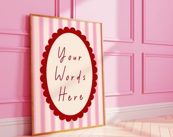 May include: A framed print with a gold border, leaning against a pink wall. The print features a cream-colored oval with the text "Your Words Here" in red, surrounded by a scalloped red border. The background has pink and white vertical stripes.