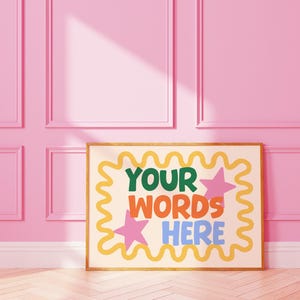 May include: A framed art print with the words "YOUR WORDS HERE" in green, orange, and blue, with pink star accents. The print has a yellow wavy border and is set against a pink wall.