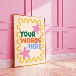 May include: A framed poster with the words "YOUR WORDS HERE" in colorful letters. The poster has a cream background with pink stars and a yellow wavy border. The frame is a light brown color.