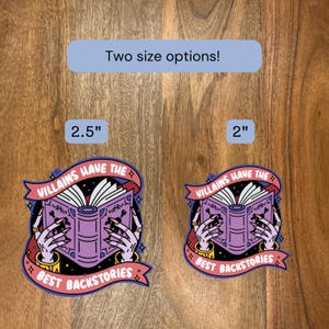 May include: Two stickers with the text "Villains Have The Best Backstories" and an illustration of a book held by hands with long nails. The stickers are available in 2.5" and 2" sizes.