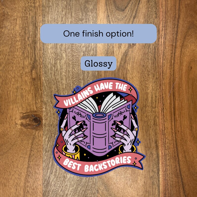 May include: Glossy sticker featuring a purple book held by hands with long, dark nails. The book's pages are open, and the sticker reads "Villains Have The Best Backstories" in a banner design. The sticker has a blue border.