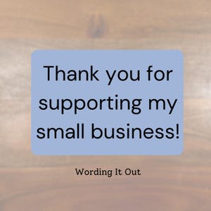 May include: A light blue rectangle with rounded corners displays the text "Thank you for supporting my small business!" in black. Below, the text "Wording It Out" is in black. The background is a wooden surface.