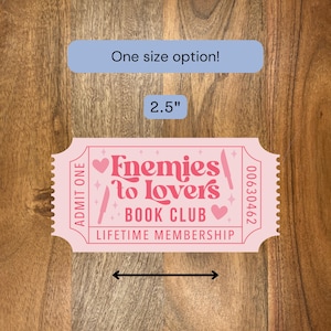 May include: A pink ticket-shaped sticker with the text "Enemies to Lovers Book Club Lifetime Membership." The sticker is 2.5 inches wide and has a blue rectangle that says "One size option!"