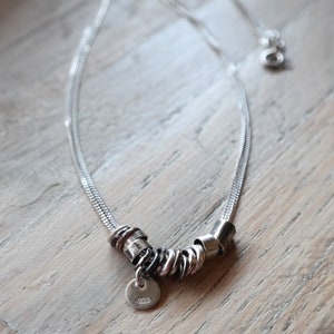May include: A silver chain necklace with a silver charm featuring multiple intertwined rings and a small round tag with the inscription ".925".