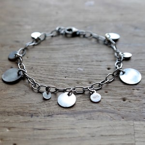 以下が含まれることがあります： 複数の丸いチャームが付いたシルバー製のチャームブレスレット。チャームの1つには「925」という数字が刻印されています。